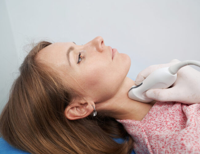 Endocrinologist wearing white gloves scanning the thyroid gland of Caucasian woman lying on couch in office